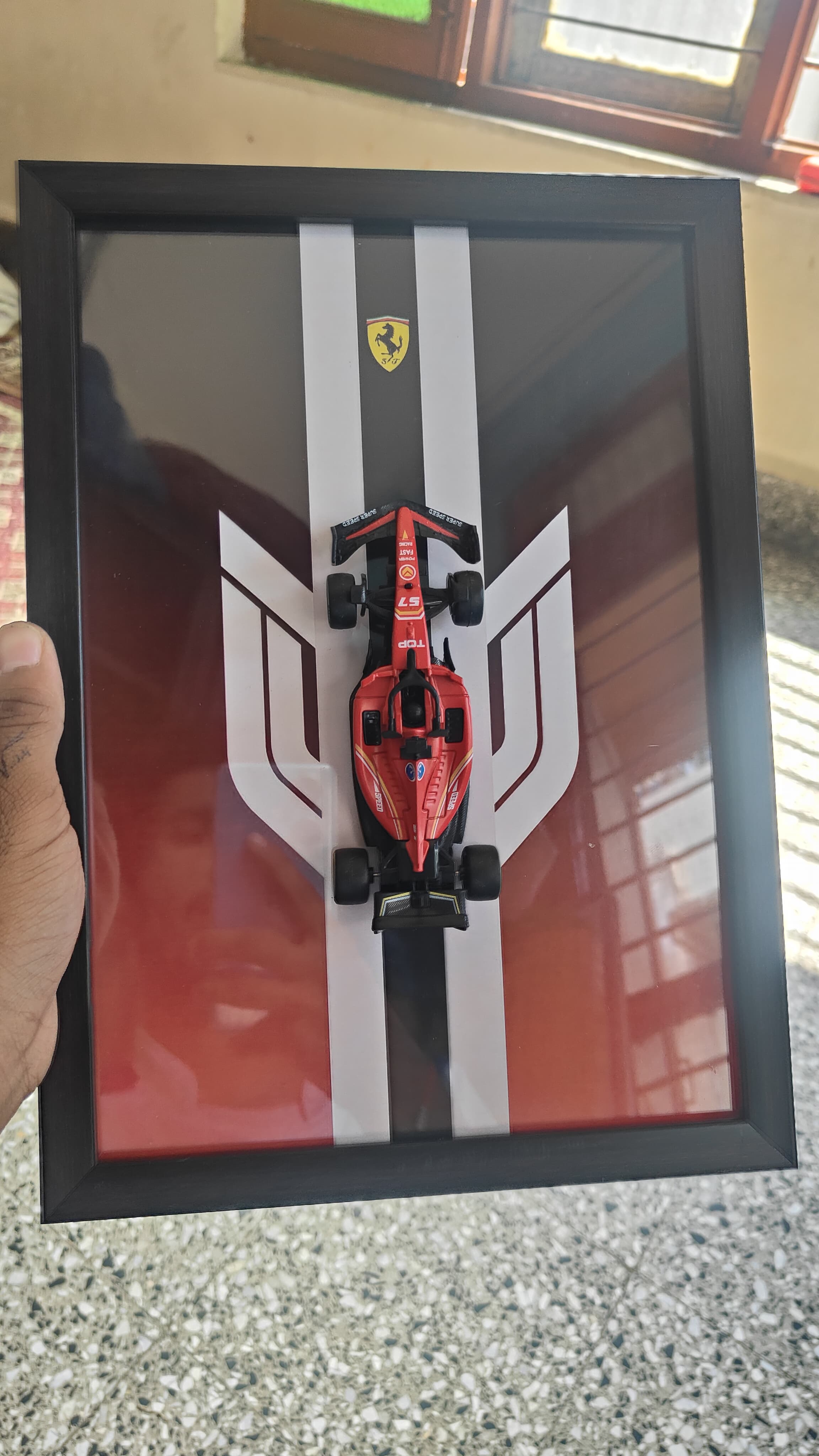 Bburago Scuderia Ferrari SF-25 red die-cast model in black shadow box with white racing stripe backdrop